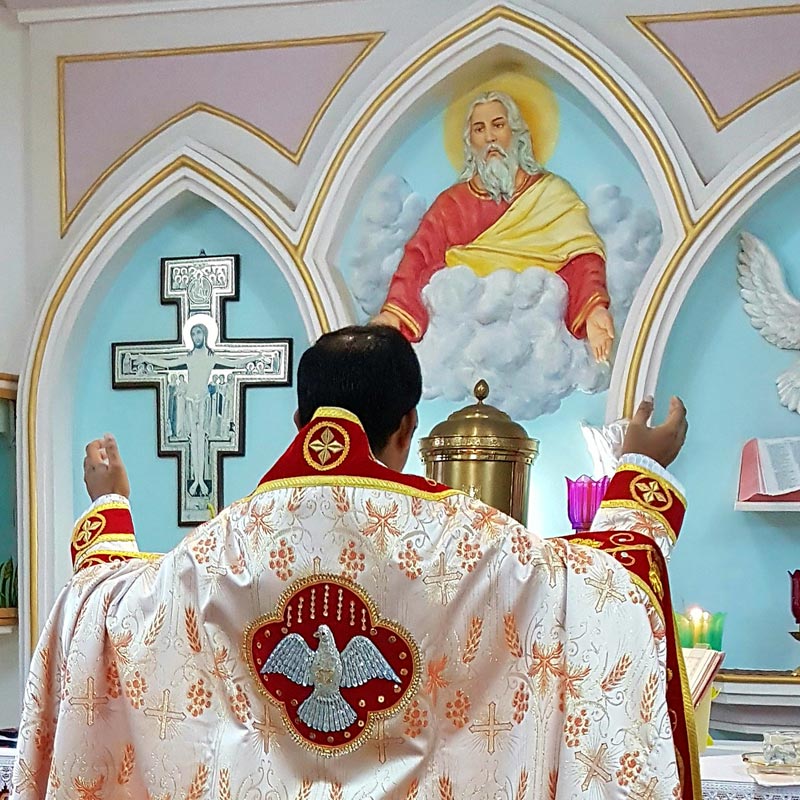 Wo Himmel und Erde sich begegnen. Ein Priester steht mit erhobenen Armen vor einem Altar und einem Wandbild Gottes in einer Kirche.