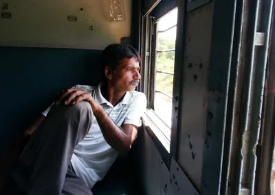 Ein Mann sitzt während einer Zugfahrt am geöffneten Fenster eines indischen Reisezuges und blickt nach draußen.
