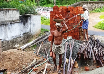 Tagelöhner trägt schwere Ziegelsteine auf einer Baustelle ohne Schutzhelm oder Sicherheitsausrüstung. Körperlich belastende Arbeit und unsichere Tageslöhne gehören für viele Menschen in Indien zum Alltag.