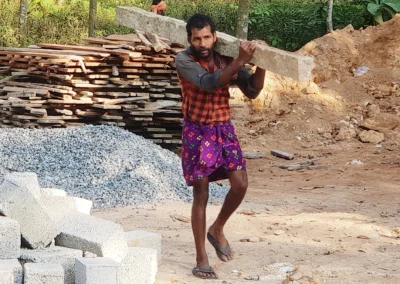 Tagelöhner trägt ohne Schutzkleidung ein schweres Betonelement auf einer Baustelle. Körperlich harte Arbeit, große gesundheitliche Risiken, extreme Hitze und unsichere Tageslöhne prägen den Alltag vieler Menschen in Armut.